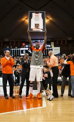 Senior center Baye Moussa Keita hoists his jersey into the air in front of a standing crowd. 
