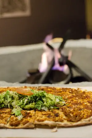 The Flame Pizza, a signature dish, is topped with ground lamb and beef, and garnished with shredded lettuce and sliced tomato.