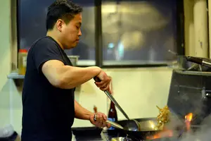 Tom Tran, owner of Sweet Basil Thai House, prepares one of his restaurant’s dishes for a customer. He typically purchases the food’s  ingredients from local markets.