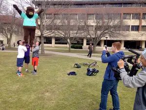 Three Syracuse University male cheerleaders hoist Yick Yack's mascot into the air. The company stopped at SU as part of its 2015 Spring Campus Tour. 
