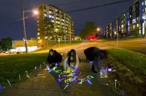 Three School of Architecture students use glow sticks to build an installation to bring awareness to crime and safety on the Syracuse University campus. The installation took place on Comstock and Euclid avenues on Tuesday and Wednesday.
