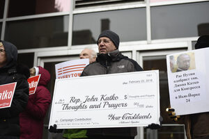 A protestor holds a check for “Thoughts and Prayers”. 