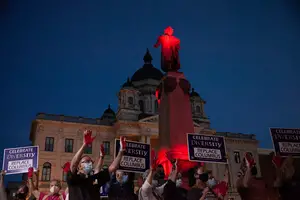 At the end of the event, organizers announced a minute of silence where attendees raised gloved hands and signs in front of the Columbus statue, illuminated in red light, to indicate he had blood on his hands.