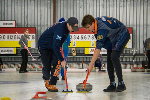 Eric Silfies (left) and Adam Wingert (right) sweep the ice in front of stone for Syracuse's club curling team.