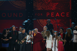 The Dalai Lama steps to the center of the stage with the One World Concert artists.