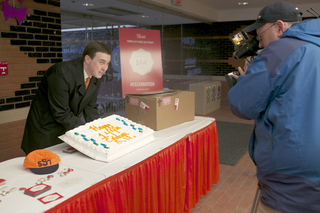 Andrew Donovan, a local channel nine news reporter lifts a SU 144th birthday cake for local news reporters to film. 144th birthday festivities, such as free cake and ice cream, began in the Schine Student Center at 10 a.m.        