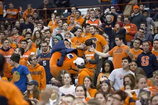 Otto the Orange walks through the student section at the Carrier Dome while a student looks at the mascot with a perplexed look on his face.