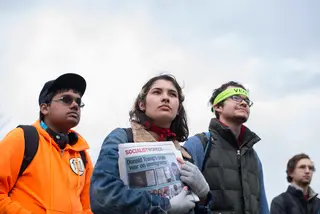 Students somberly listen to speakers at the rally. One student holds a newspaper related to socialism.