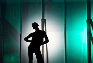 A model in the Fasion and Design Society 2021 Fall/Winter fashion show stands backlit before taking to the stage. 