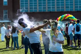 Two students throw powder at each other covering the one another in a variety of colors. 