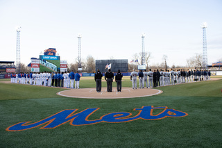 Players line the sides of the diamond as the colors are presented and the National Anthem is played. 
