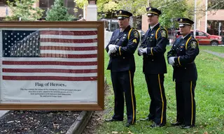 Officers from the Syracuse Police Department stand alongside the Flag of Heroes. The flag is detailed with the names of emergency personnel that gave their lives to save others during the 9/11 terrorist attacks. 