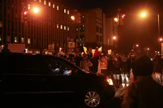 A car attempts to drive by the marchers at the intersection in front of the Patrick J. Corbett Justice Center.